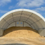 Large fabric hoop building storing road salt and sand, featuring a protective covered structure designed for municipal winter material storage