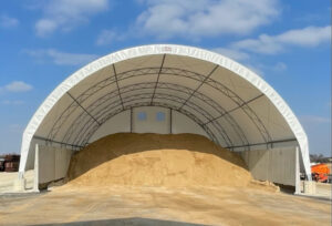 Large fabric hoop building storing road salt and sand, featuring a protective covered structure designed for municipal winter material storage